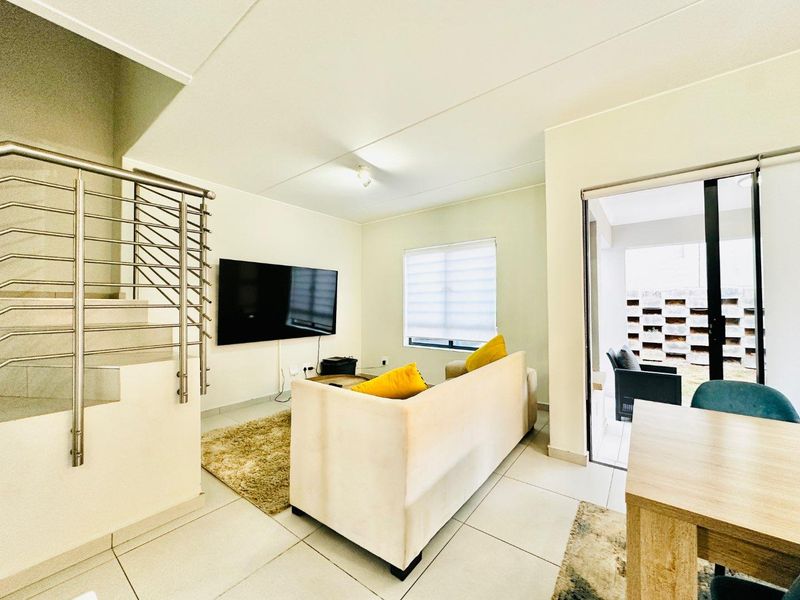 Open-plan living area featuring tiled floors, a modern stainless steel staircase railing, and direct access to an outdoor patio through sliding glass doors.