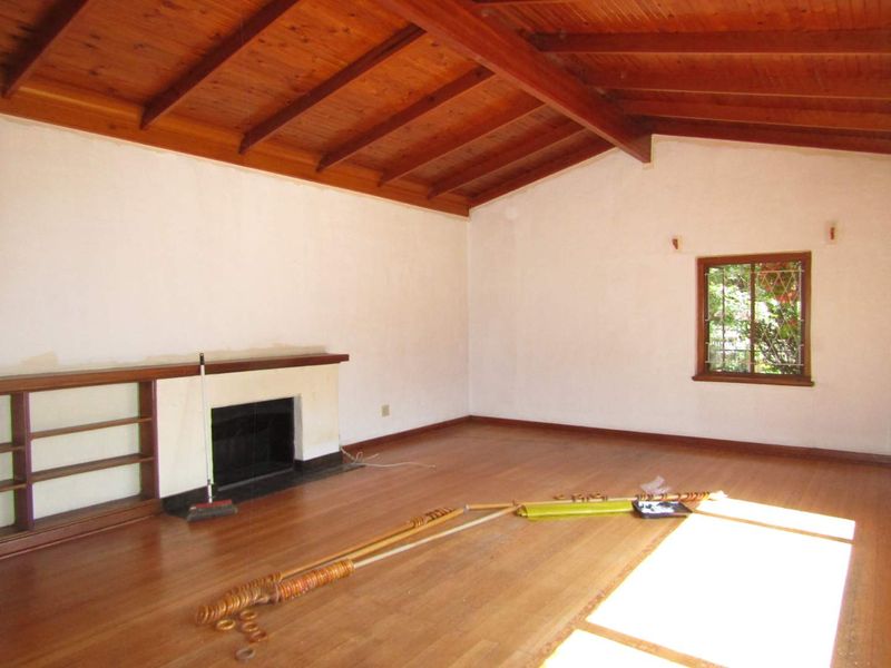 Spacious living room featuring a vaulted timber beam ceiling, hardwood floors, a built-in fireplace, and integrated shelving, offering a bright and versatile living space.
