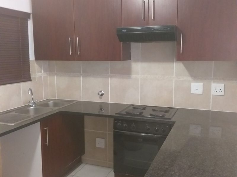 A functional kitchen featuring dark wood cabinetry, granite countertops, a built-in electric stove with extractor fan, and a stainless steel double sink.