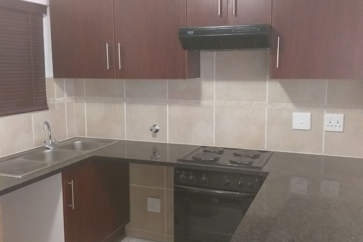 A functional kitchen featuring dark wood cabinetry, granite countertops, a built-in electric stove with extractor fan, and a stainless steel double sink.