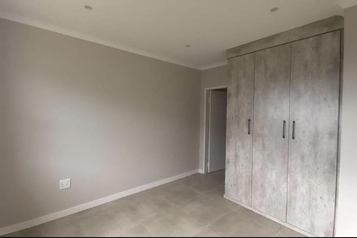 A clean, modern bedroom featuring neutral wall tones, large format floor tiles, and contemporary built-in cupboards with a textured finish.