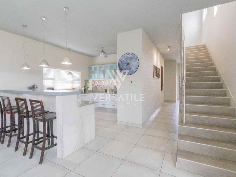 Open-plan living area featuring a kitchen with island, tiled flooring, and a staircase with a stainless steel handrail.