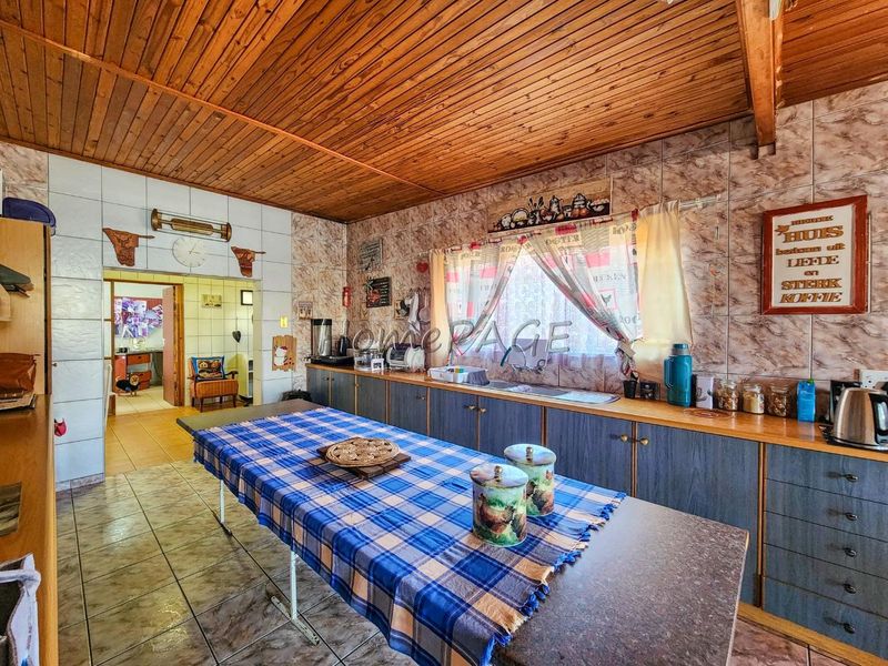 A functional kitchen featuring extensive built-in cabinetry, laminate countertops, a double basin sink, and a distinctive timber tongue and groove ceiling.
