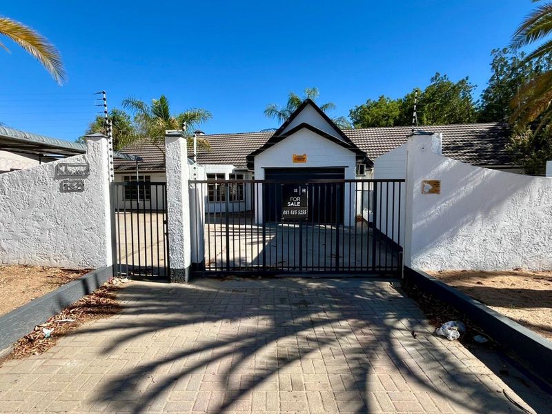 Front exterior view of the property featuring a paved driveway, secure metal gate, electric fencing, and a tiled roof garage entrance.