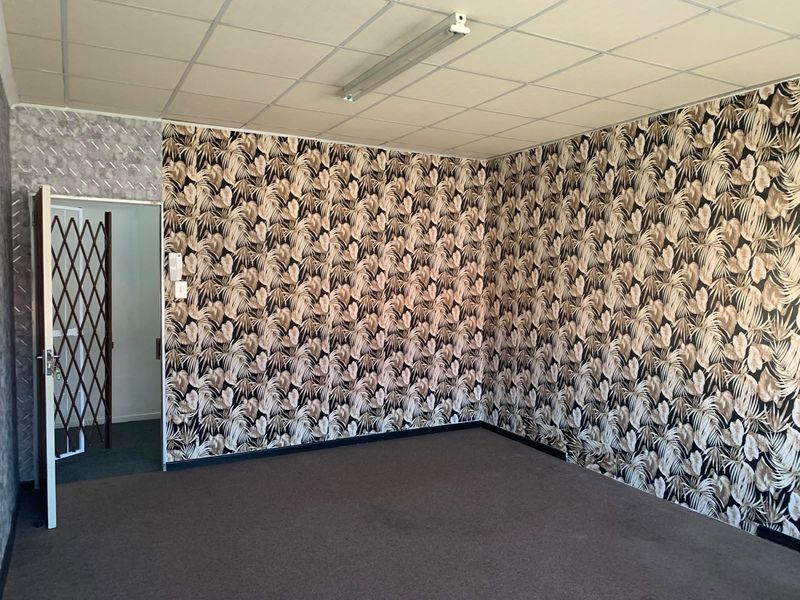 An empty office space featuring a suspended ceiling, patterned wallpaper, and carpet flooring, accessible via a security gate.