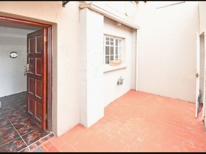 A small, enclosed outdoor patio area featuring terracotta tiled flooring, an exterior wall light, and access to the interior through a timber door.