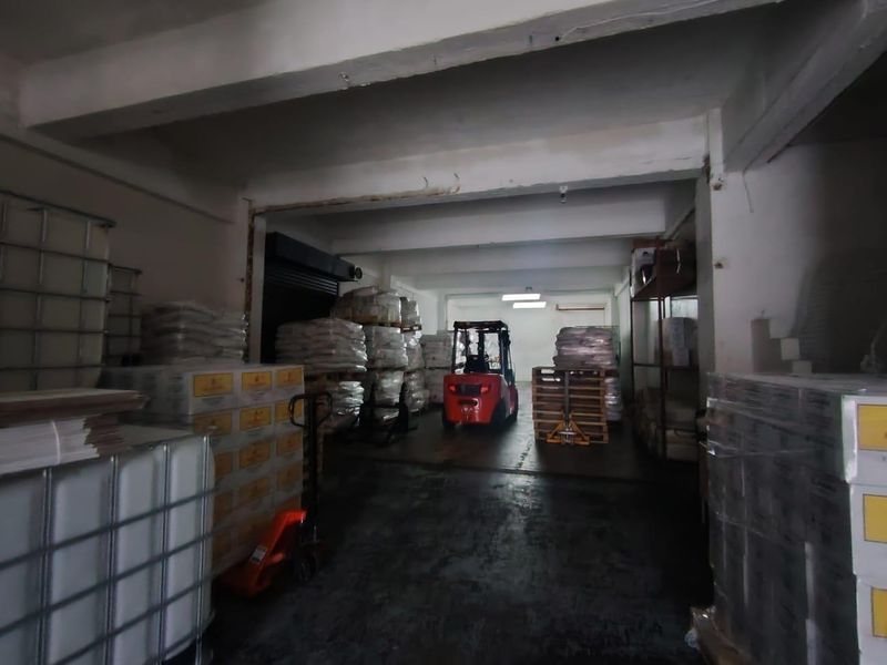 Industrial warehouse or storage space featuring concrete flooring, exposed structural beams, and a roller shutter door, currently utilized for inventory storage.
