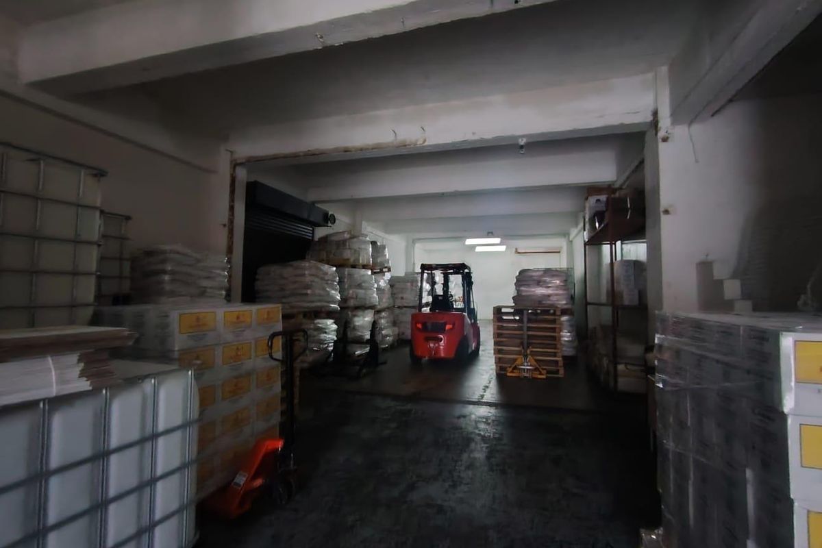 Industrial warehouse or storage space featuring concrete flooring, exposed structural beams, and a roller shutter door, currently utilized for inventory storage.