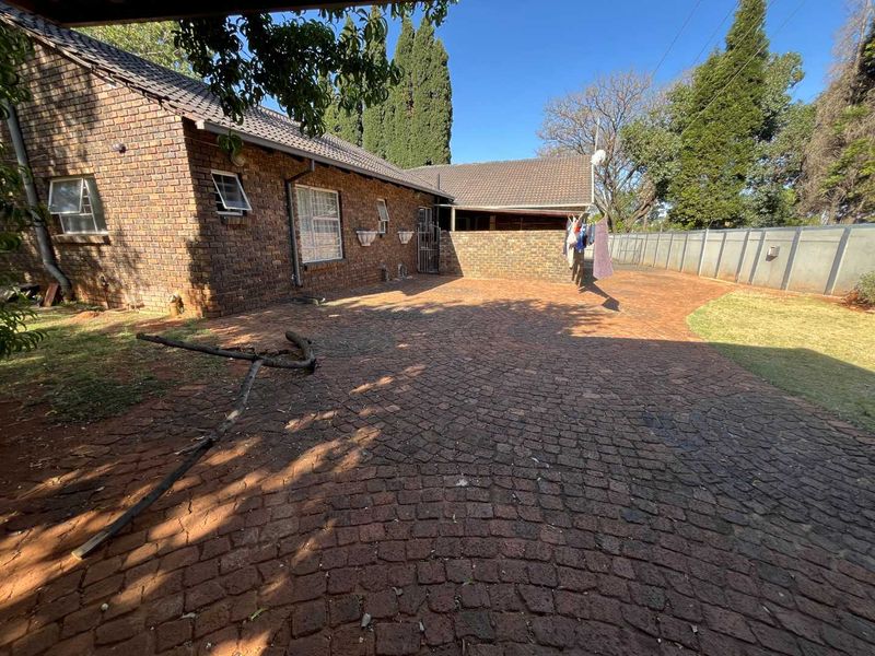 Rear exterior view of the property featuring a large brick-paved courtyard, facebrick facade, and perimeter precast concrete walling.