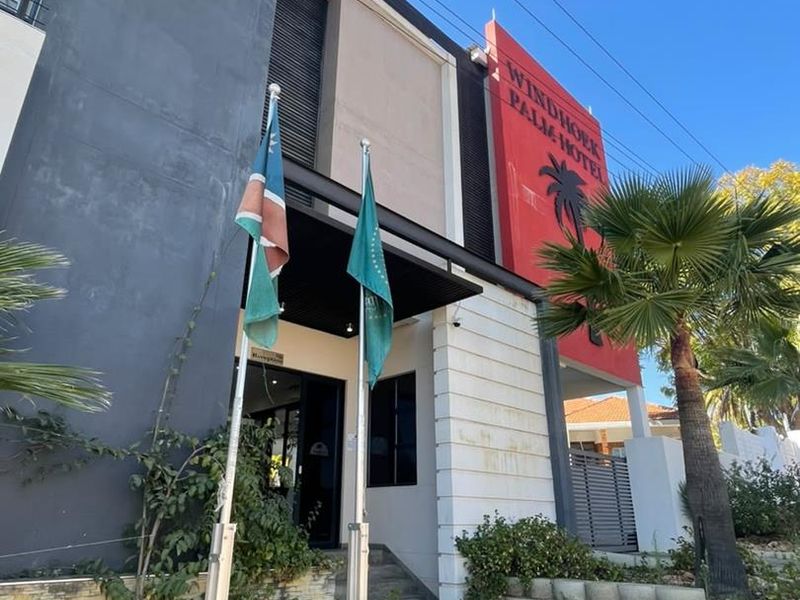 Front facade of the Windhoek Palm Hotel featuring modern architectural elements, signage, flagpoles, and a paved entrance walkway.