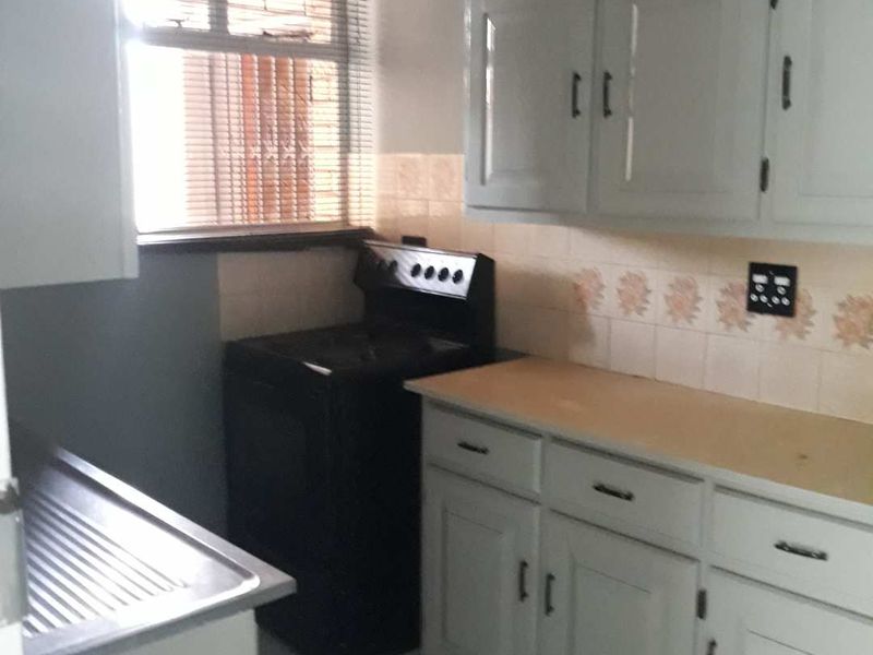 A compact kitchen featuring white cabinetry, laminate countertops, a stainless steel sink, and a freestanding stove with a tiled backsplash.