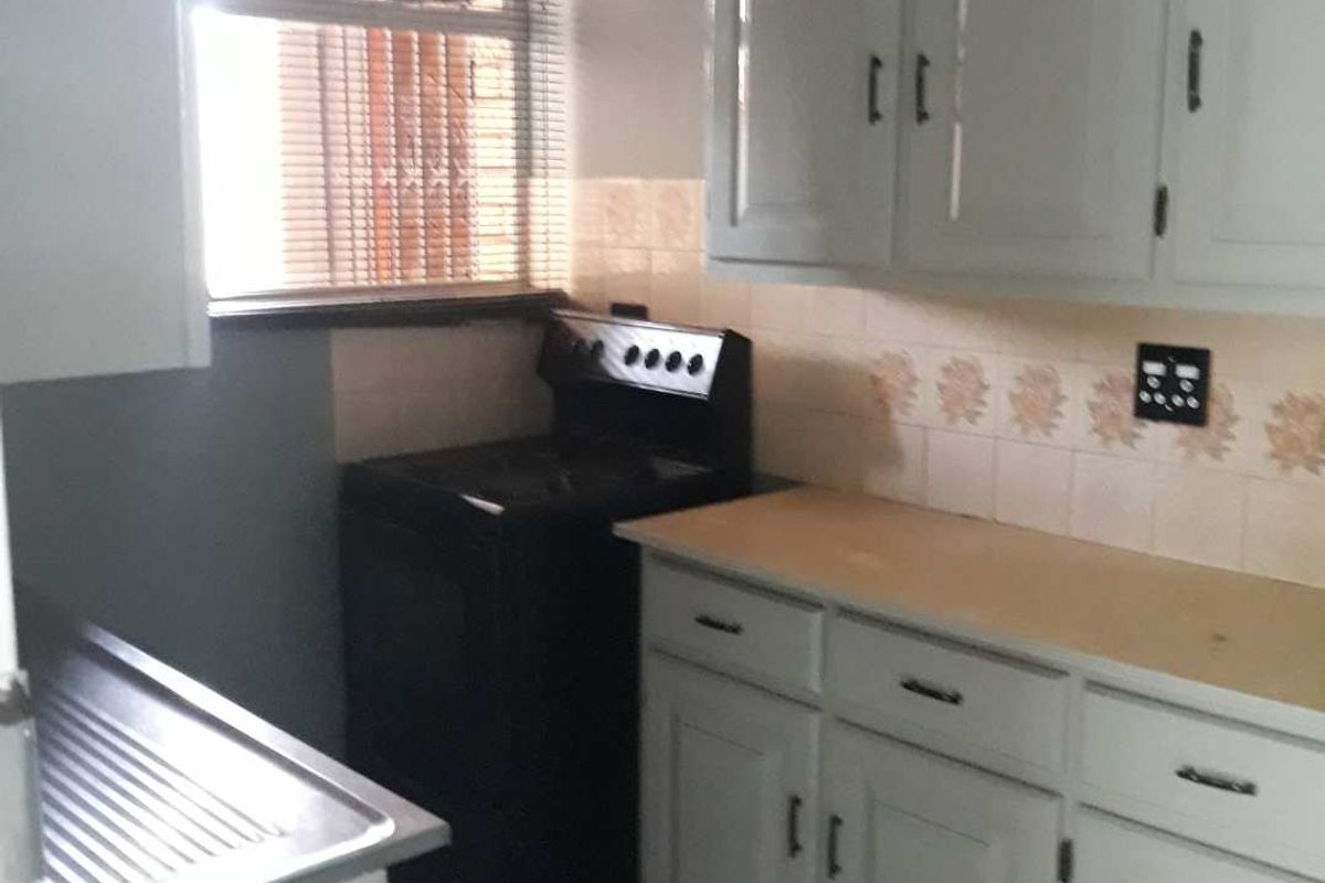 A compact kitchen featuring white cabinetry, laminate countertops, a stainless steel sink, and a freestanding stove with a tiled backsplash.