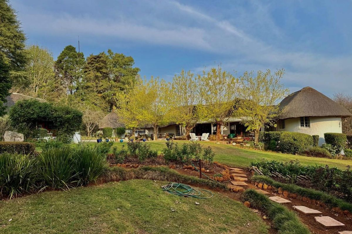 A view of the rear garden featuring a well-maintained lawn, stone pathway, and the rear elevation of a farmhouse with a traditional thatch roof.