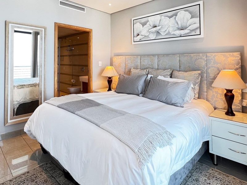 A well-maintained bedroom featuring tiled flooring, a large upholstered headboard, and direct access to an en-suite bathroom with modern finishes.