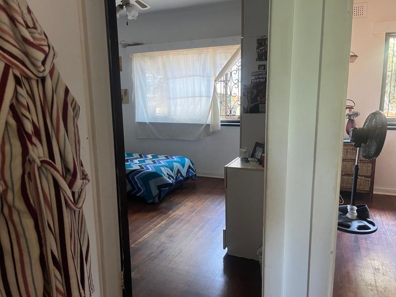 A bedroom featuring timber flooring and security bars on the windows, viewed from an adjacent hallway.