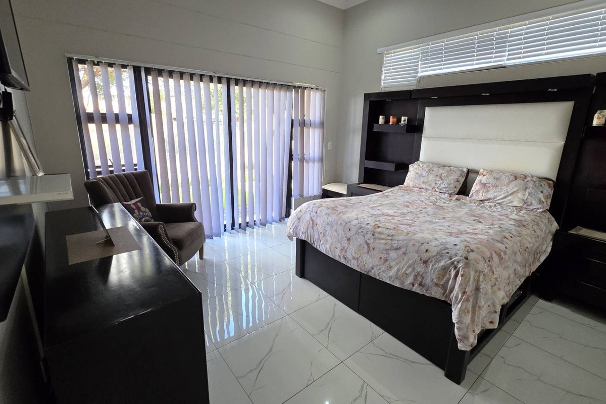 Spacious bedroom featuring modern white marble-look floor tiles, large sliding glass doors with vertical blinds, and integrated headboard cabinetry.