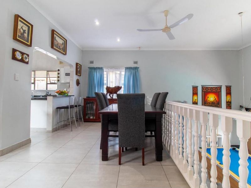 Open-plan dining area featuring tiled floors, a ceiling fan, and a breakfast counter overlooking the kitchen, with a balustrade bordering the lower level.
