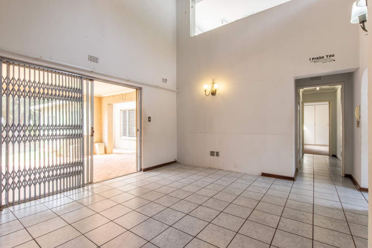 Spacious living area with high ceilings, tiled flooring, and a sliding security gate leading to an outdoor patio.