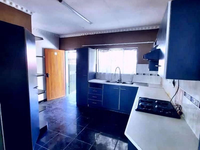 A functional kitchen featuring dark cabinetry, a built-in hob with extractor fan, double sink, and dark tiled flooring with direct access to the exterior.