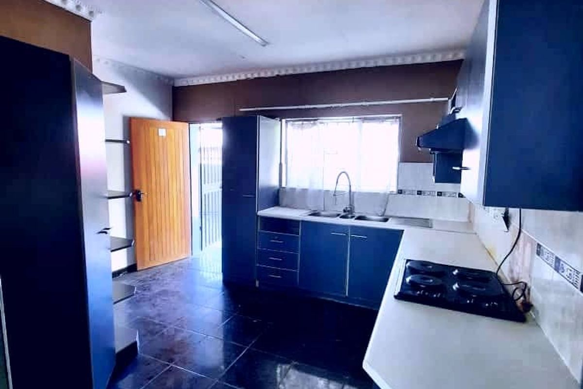 A functional kitchen featuring dark cabinetry, a built-in hob with extractor fan, double sink, and dark tiled flooring with direct access to the exterior.