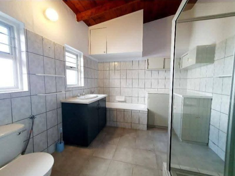 Spacious bathroom featuring a bathtub, separate shower enclosure, vanity basin, and built-in storage cupboards with exposed timber ceiling beams.
