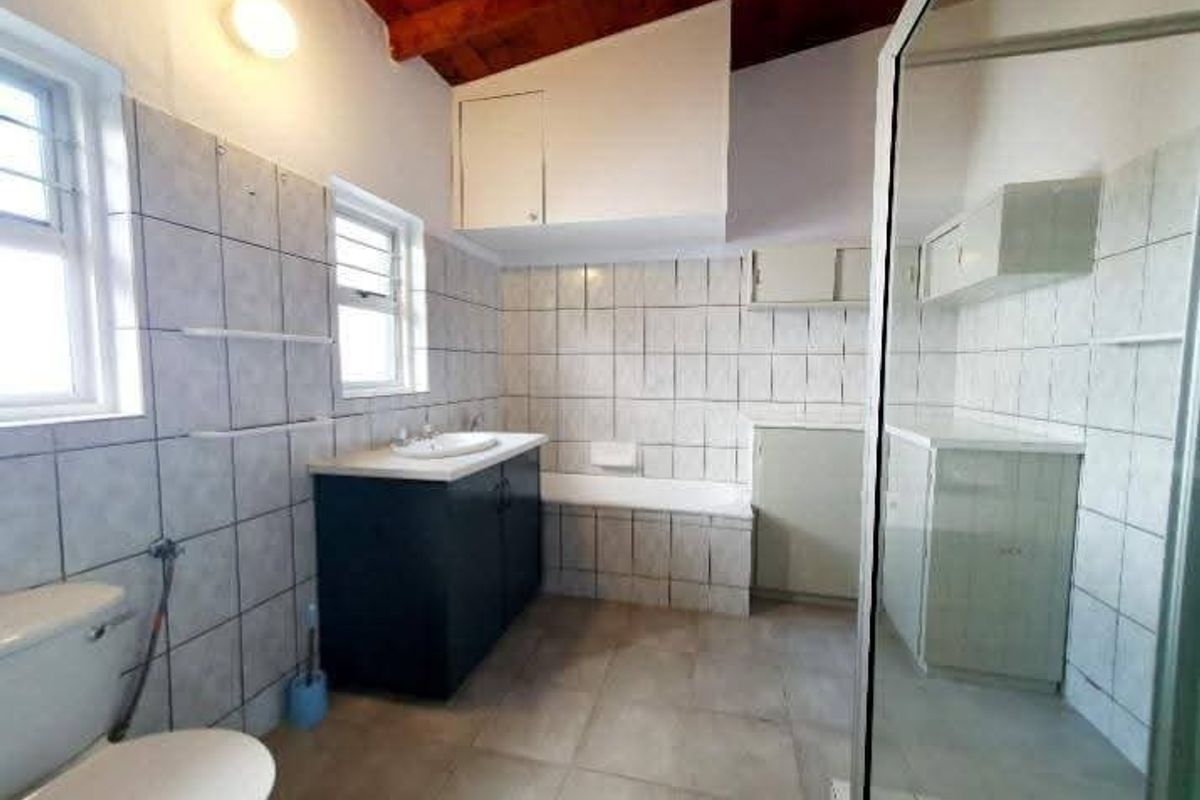 Spacious bathroom featuring a bathtub, separate shower enclosure, vanity basin, and built-in storage cupboards with exposed timber ceiling beams.