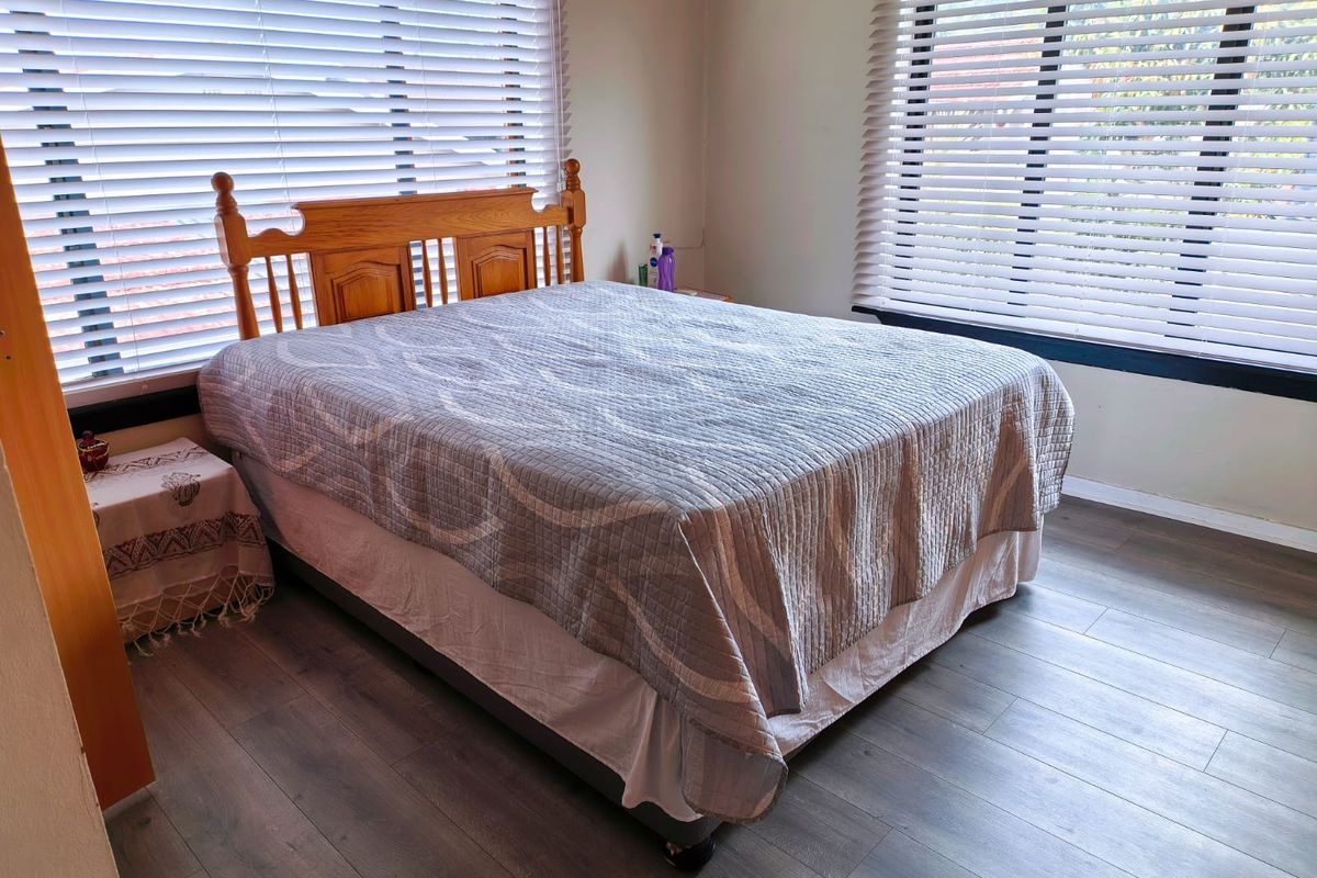 A bedroom featuring laminate flooring and dual windows fitted with venetian blinds.