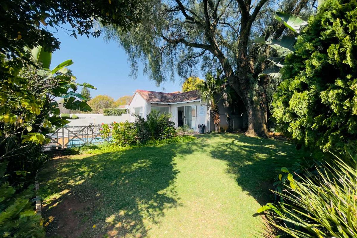 A view of the rear garden featuring a well-maintained lawn, mature trees, and a swimming pool adjacent to the main building structure.