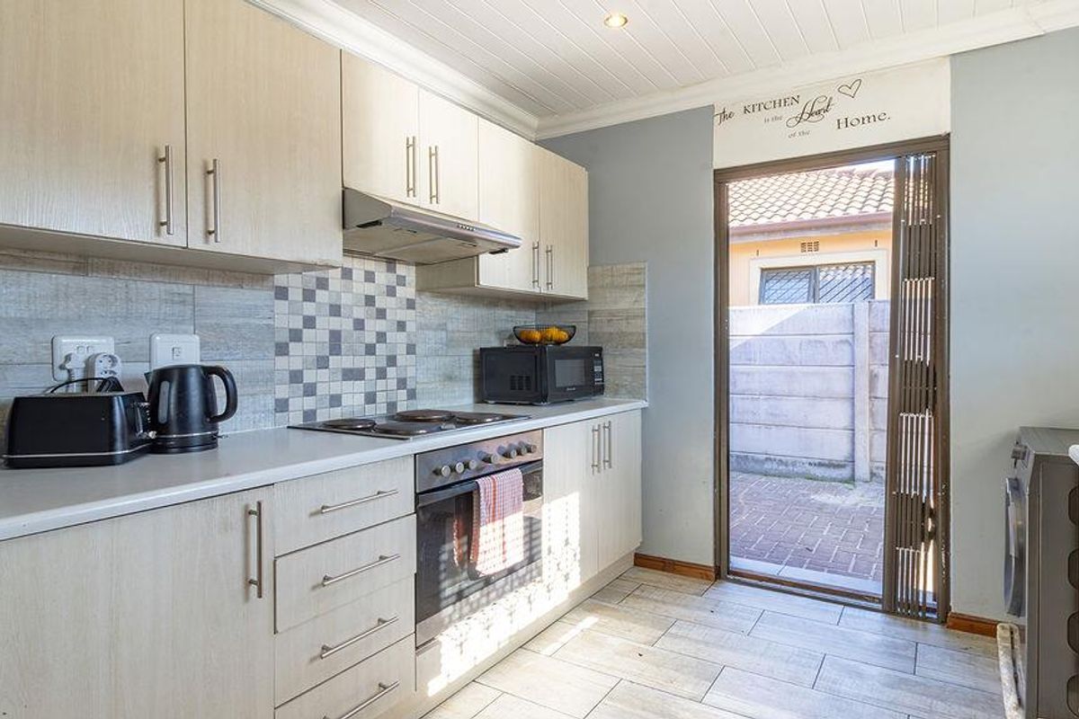 Functional kitchen featuring light wood-finish cabinetry, built-in oven and hob, tiled backsplash, and direct access to the rear exterior area.