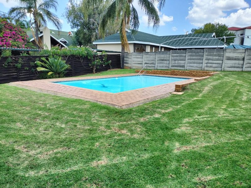 A private backyard featuring a rectangular swimming pool with brick coping, surrounded by a well-maintained lawn and secure boundary fencing.