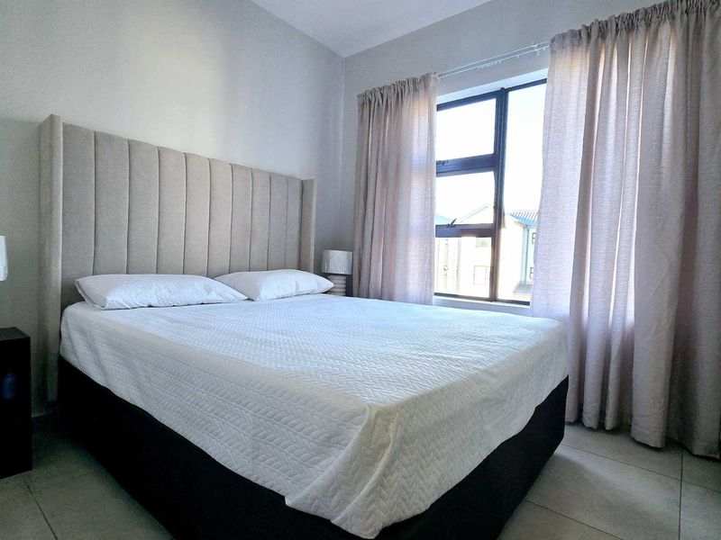 A well-maintained bedroom featuring neutral wall tones, tiled flooring, and a large window with natural light.