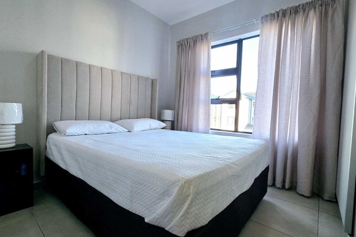 A well-maintained bedroom featuring neutral wall tones, tiled flooring, and a large window with natural light.