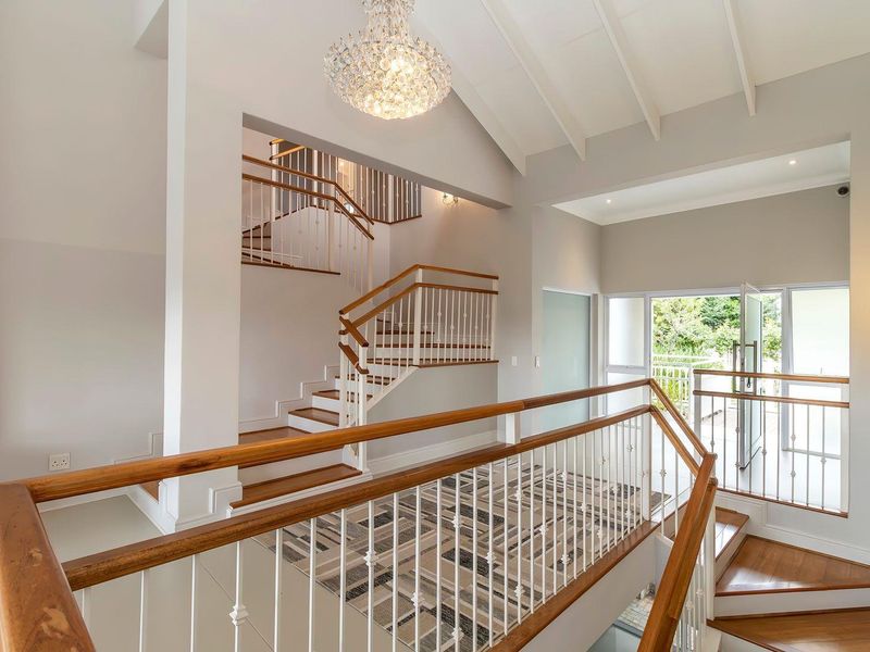 Spacious double-volume entrance hall featuring a grand staircase with timber handrails, vaulted ceilings, and elegant chandelier lighting.