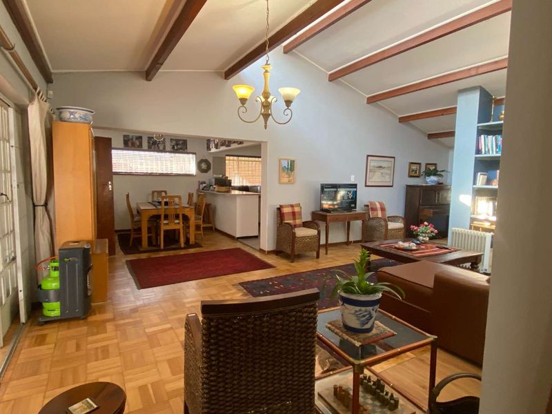 Spacious open-plan living and dining area featuring exposed timber ceiling beams, classic parquet flooring, and a built-in shelving unit.