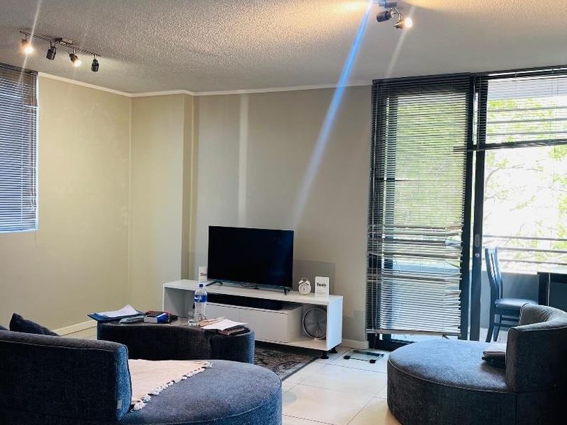 A living room featuring tiled flooring, track lighting, and a sliding glass door leading to a balcony with venetian blinds.