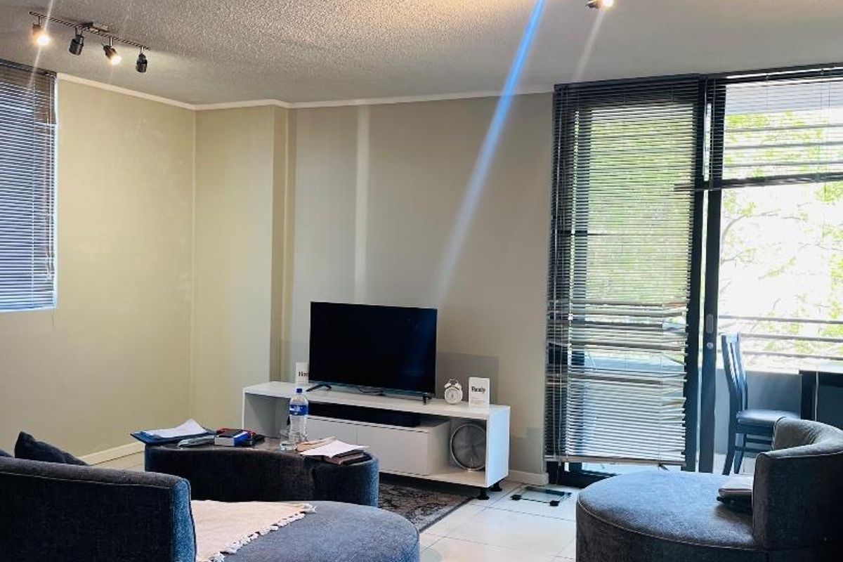 A living room featuring tiled flooring, track lighting, and a sliding glass door leading to a balcony with venetian blinds.