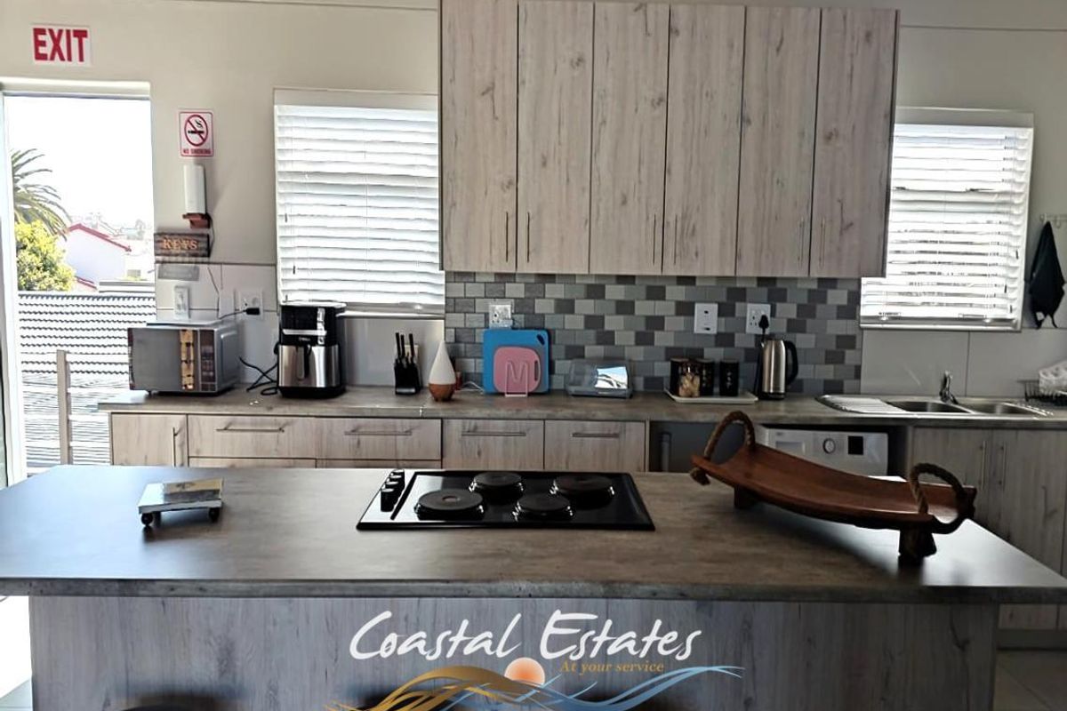 Modern kitchen featuring light wood-grain cabinetry, a central island with a built-in electric hob, and a mosaic tile backsplash.