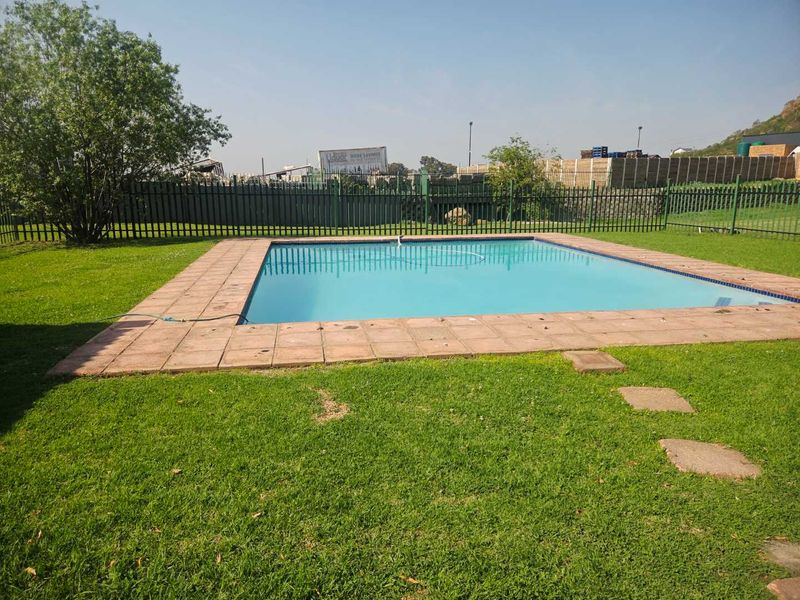 Outdoor swimming pool area featuring a paved surround, surrounding lawn, and perimeter fencing.