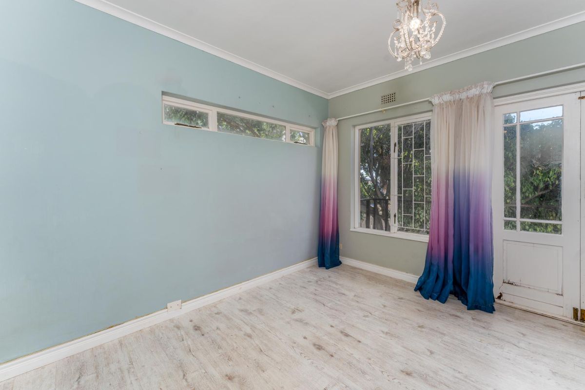 A bright bedroom featuring light wood-look flooring, a large window with security bars, and a glass-paneled door providing direct access to the exterior.