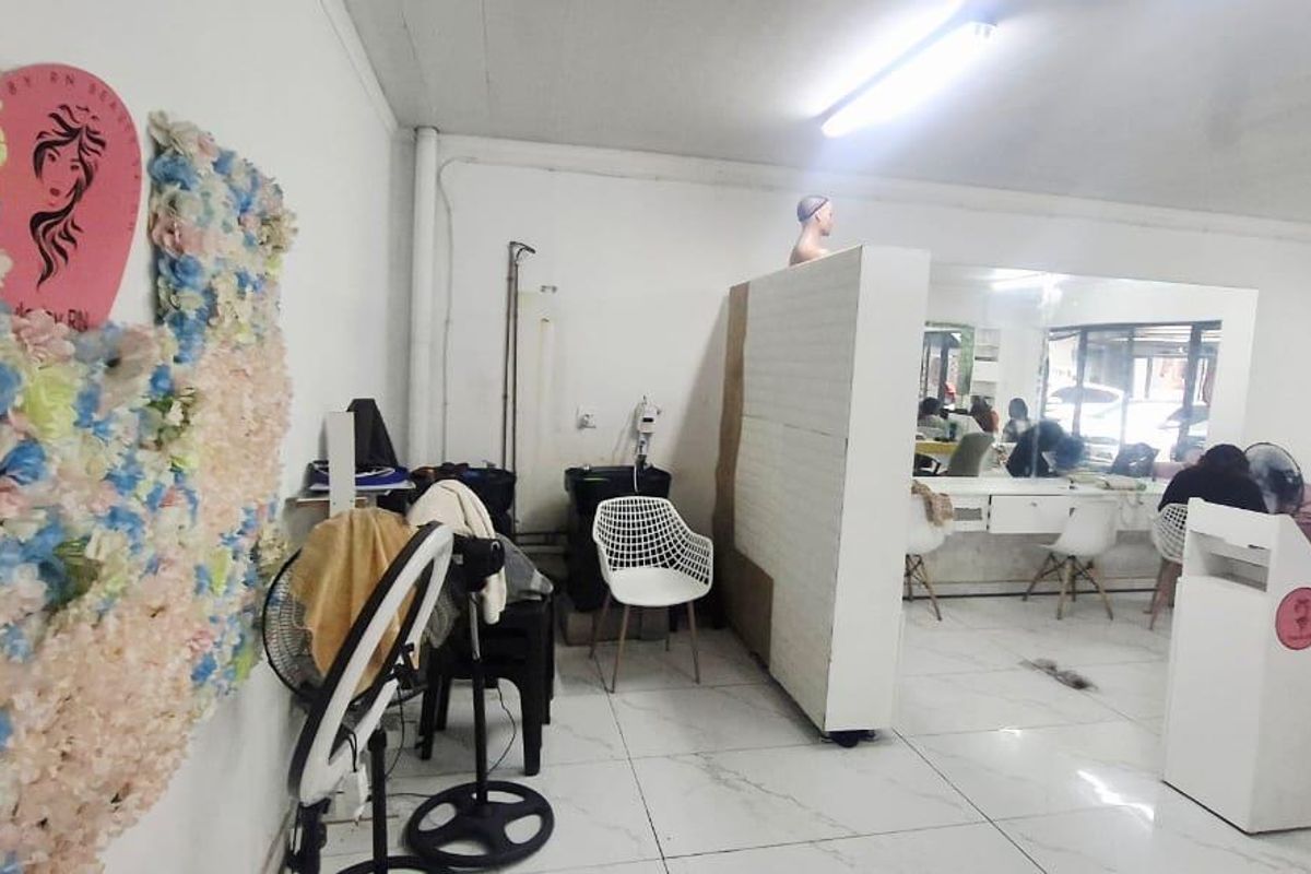A commercial salon space featuring tiled flooring, a central partition wall, and built-in vanity mirrors, suitable for beauty or professional services.