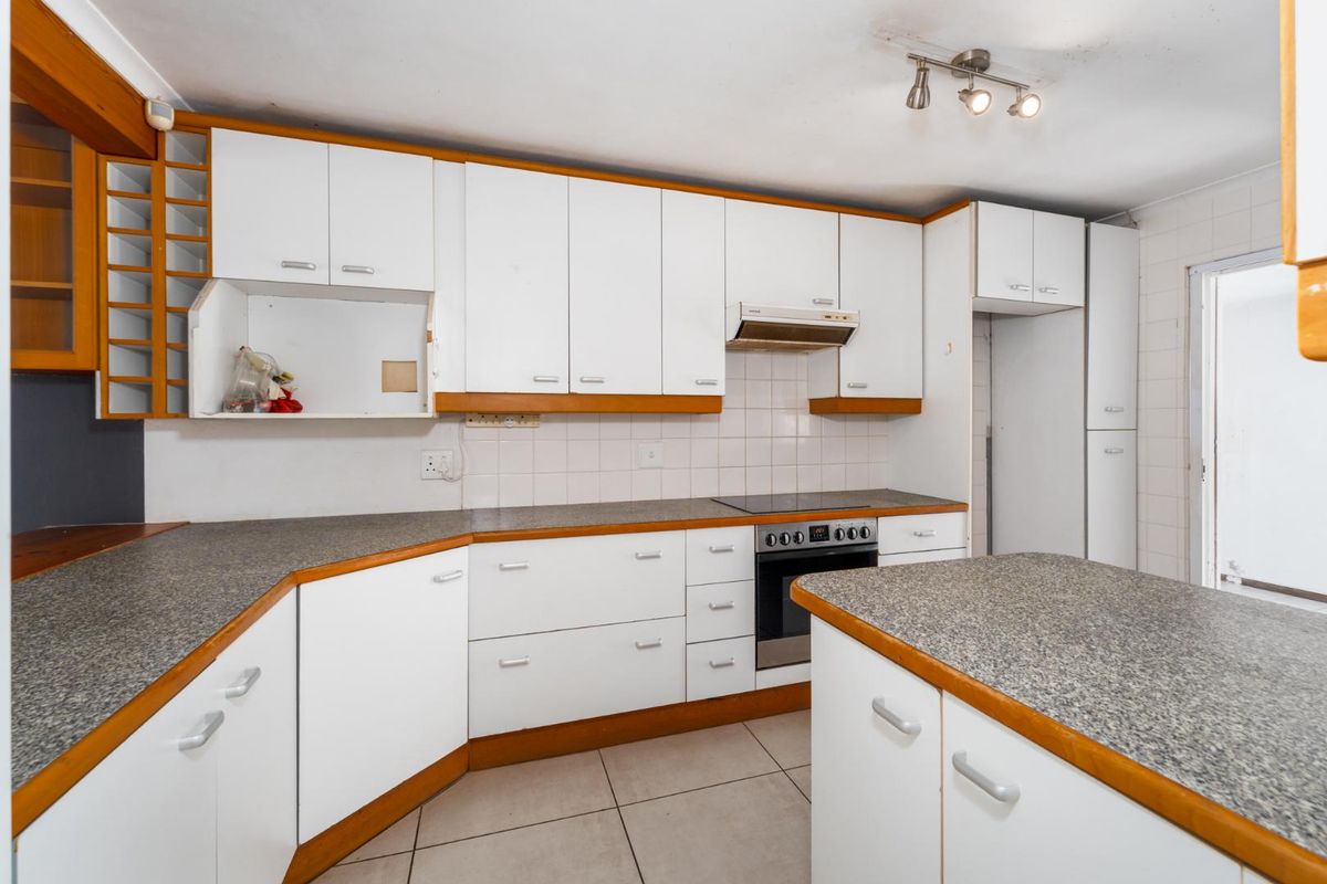 A functional kitchen featuring white cabinetry with wood trim, granite-look countertops, built-in oven, hob, and tiled flooring, offering a blank canvas for renovation.