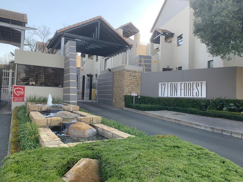 The entrance to 17 on Forest apartment complex, featuring a modern security gate, stone-clad water feature, and well-maintained landscaped gardens.