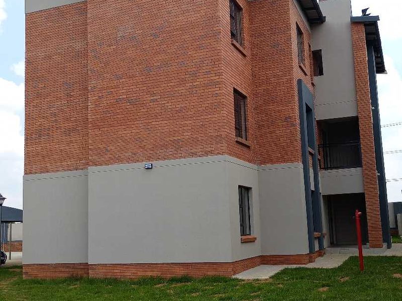 A view of the rear elevation of a multi-story townhouse featuring a combination of face brick and plastered finishes with a paved walkway.