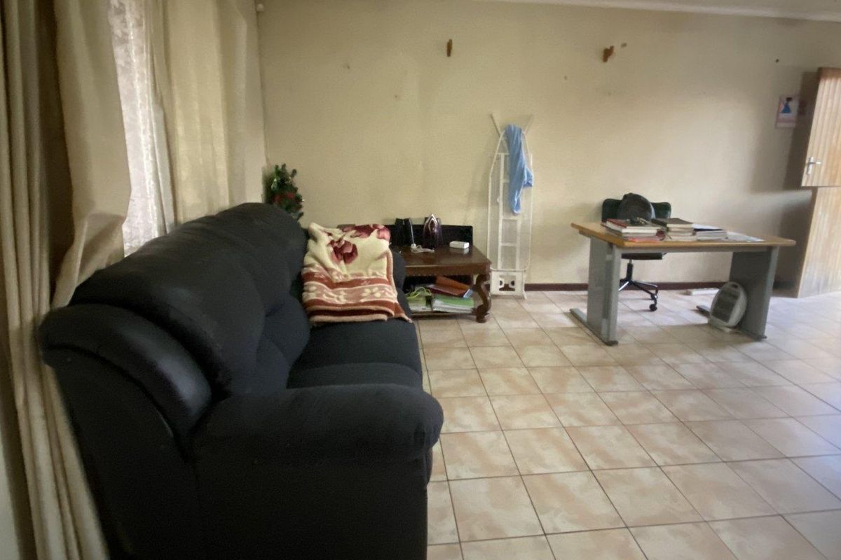 A living room area featuring ceramic floor tiles and curtain rails, showing signs of wear on the walls requiring maintenance and cosmetic updates.