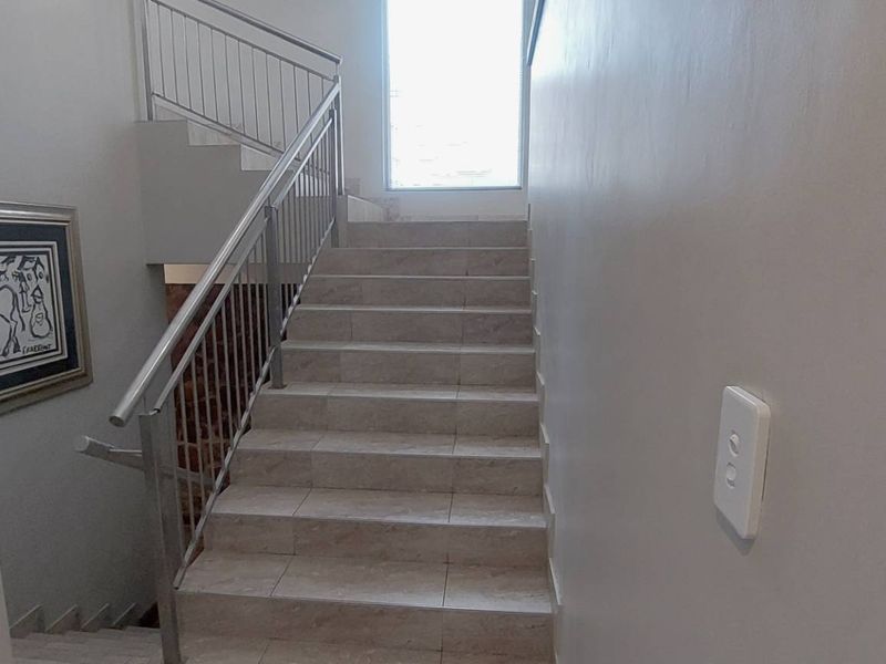 A clean, modern staircase featuring tiled steps and a stainless steel balustrade, providing a bright and functional transition between levels.