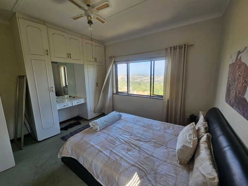 A bedroom featuring built-in cupboards with an integrated vanity, a ceiling fan, and a window offering elevated views.