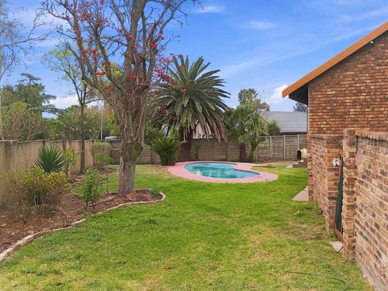A private backyard featuring a kidney-shaped swimming pool with a paved surround, set within a landscaped garden enclosed by brick boundary walls.