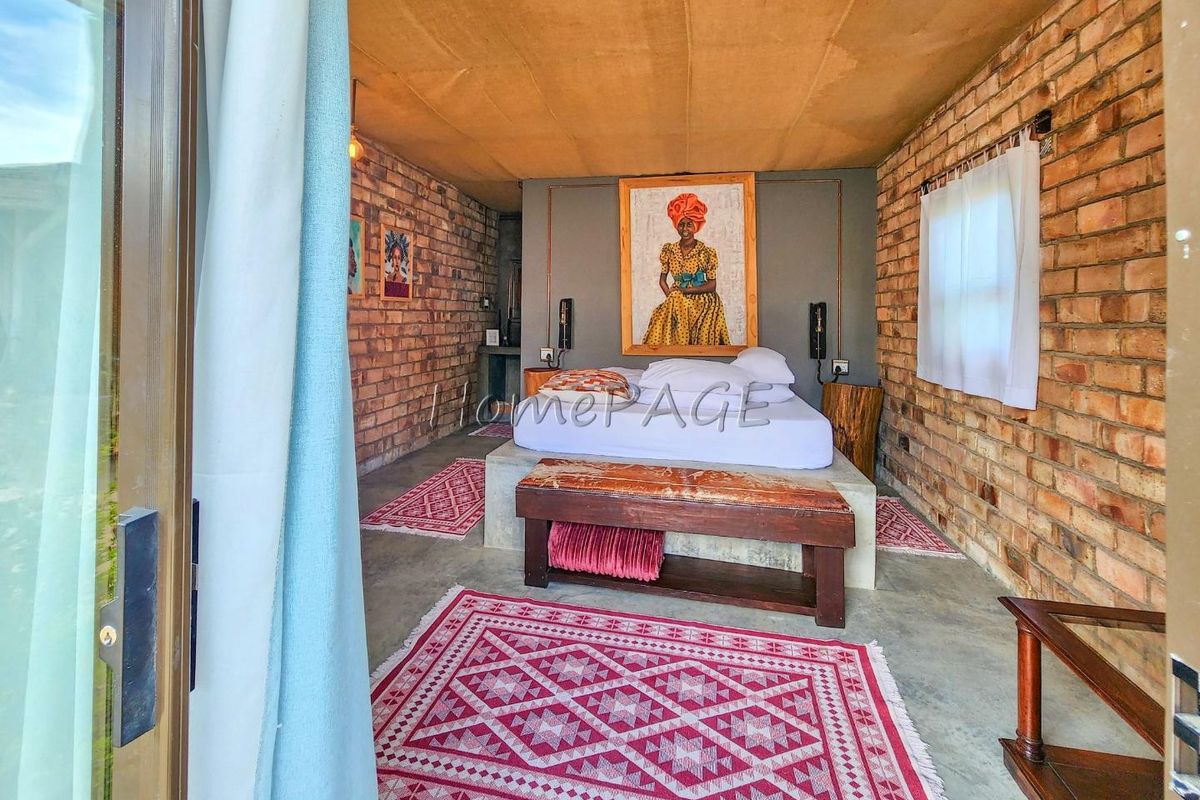 A rustic bedroom featuring exposed brick walls, a concrete floor, and a built-in concrete bed base, offering a unique industrial aesthetic.
