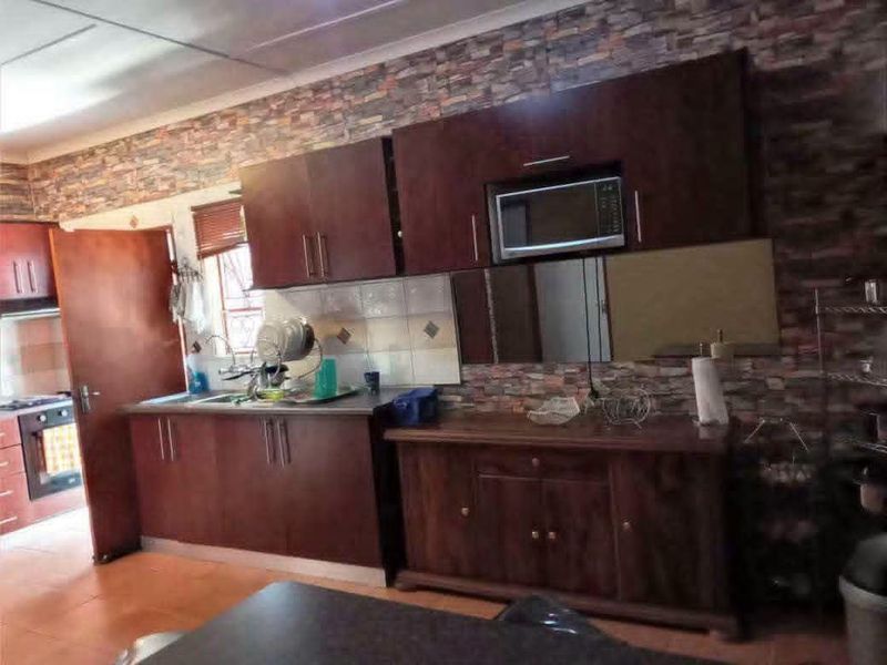 A functional kitchen featuring dark wood cabinetry, tiled backsplash, and built-in microwave, with stone-effect wall cladding and ceramic floor tiles.