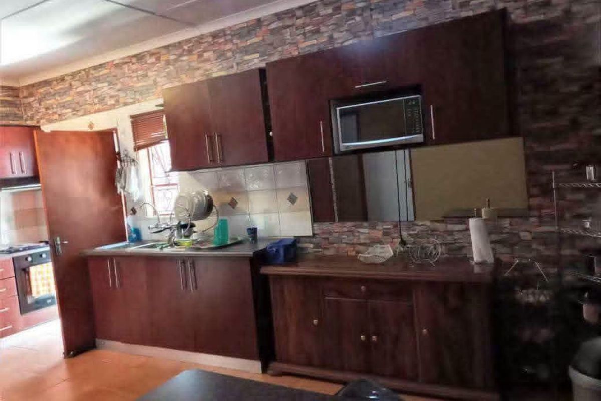 A functional kitchen featuring dark wood cabinetry, tiled backsplash, and built-in microwave, with stone-effect wall cladding and ceramic floor tiles.